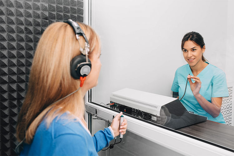 A woman taking a hearing test at a hearing care clinic. An audiologist or hearing care specialist is conducting the test.