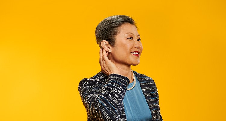 Woman wearing Philips HearLink and smiling while she touches her hearing aid that makes her hear better.