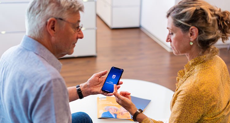 Man wearing Philips HearLink hearing aids in a counselling session with a female hearing care specialist, learning to use the Philips HearLink app
