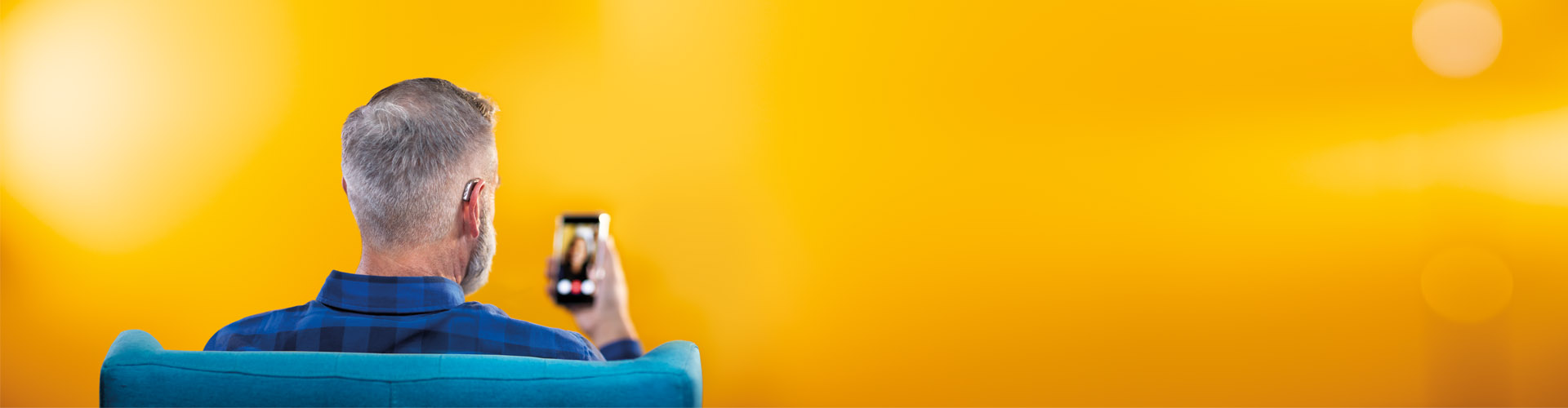 Hombre de mediana edad que usa su teléfono inteligente y sus audífonos HearLink de Philips para conectarse con amigos haciendo una videollamada.