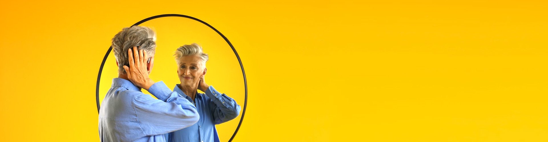Une femme souriante qui porte un appareil auditif Philips HearLink et qui se regarde dans le miroir