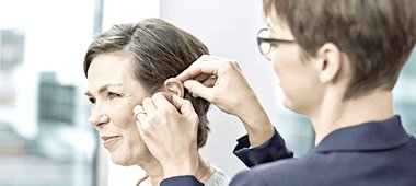 Une audioprothésiste pose une prothèse auditive sur l'oreille d'un client
