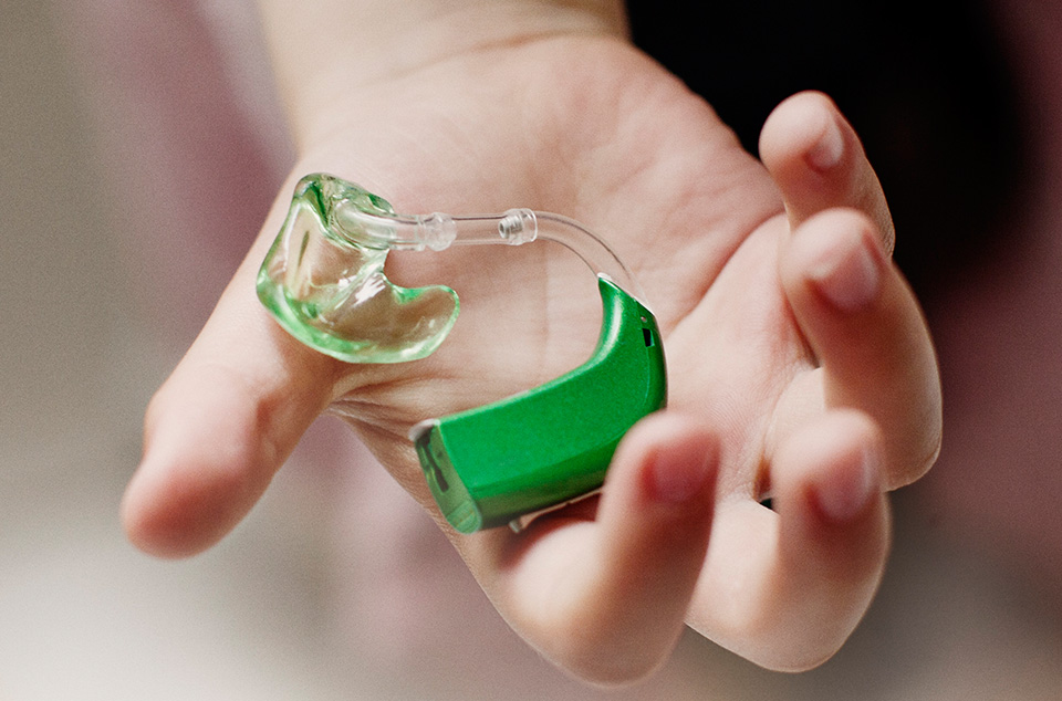 appareil auditif pour enfant de couleur verte présenté dans la main de l'enfant