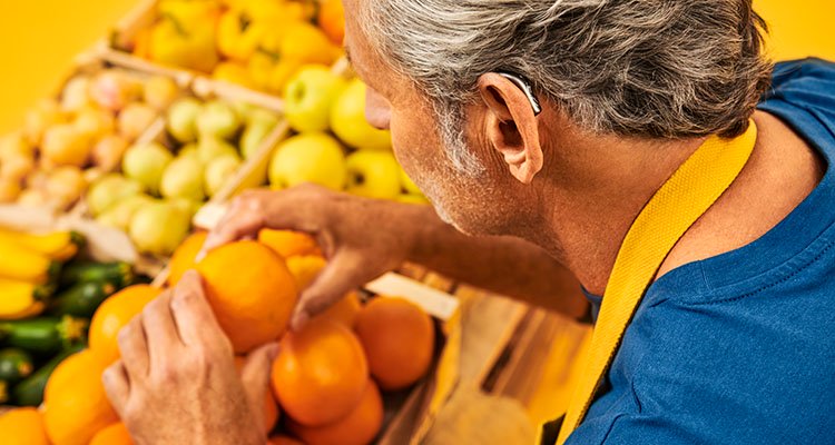 フィリップス ヒアリンクの充電式補聴器を装用した男性が、ファーマーズマーケットでオレンジを投げて孫と会話