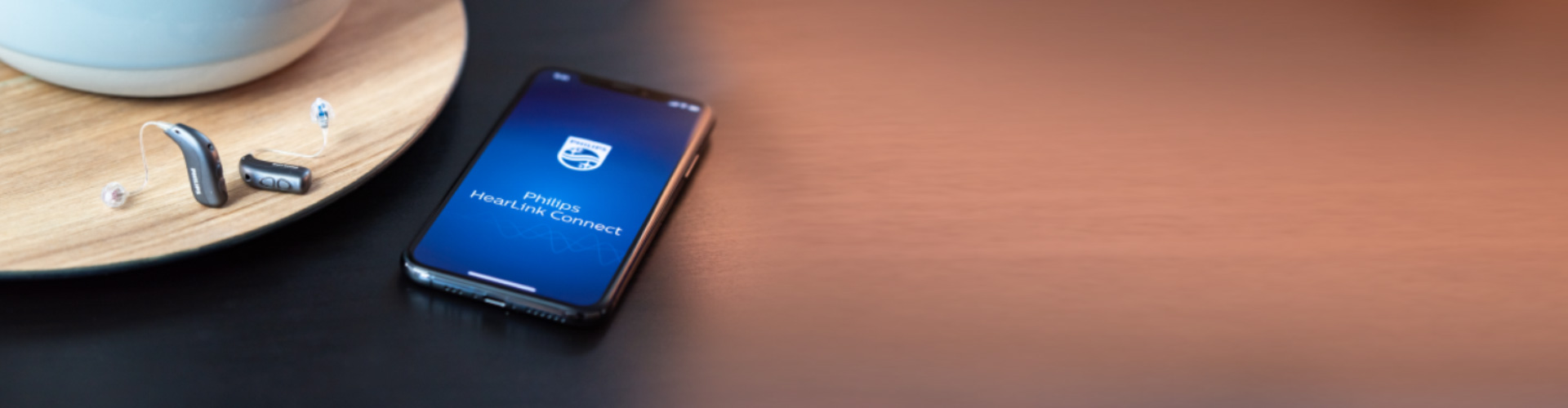 Philips HearLink Connect アプリを開いたスマートフォンとフィリップス ヒアリンク補聴器