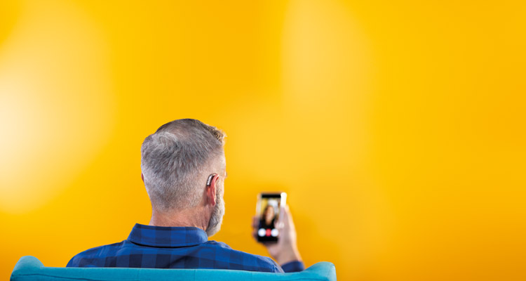 Man van middelbare leeftijd gebruikt zijn smartphone en zijn Philips HearLink hoortoestellen om te verbinden met vrienden door het houden van een videogesprek.