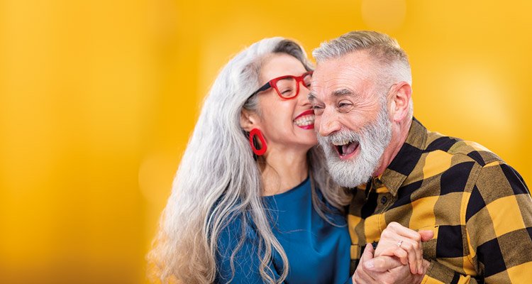 Een vrouw van middelbare leeftijd omhelst een vriend en fluistert met hem. Hij draagt Philips HearLink oplaadbare hoortoestellen.