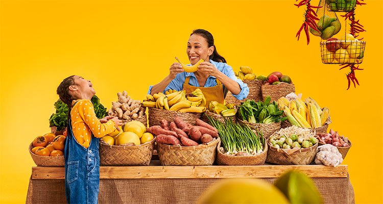 Vrouw met Philips HearLink hoortoestellen creërt een glimlach met een banaan om haar kleindochter op te fleuren op een boerenmarkt