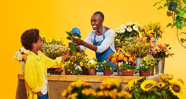 Vrouw met Philips HearLink hoortoestellen krijgt een blauwe bloem van haar kleinzoon als cadeau op een bloemenmarkt