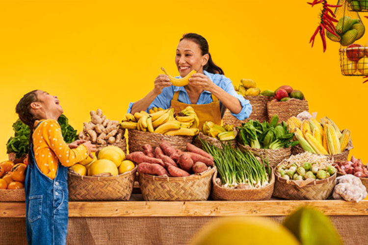 En kvinna med Philips HearLink hörapparater gör ett roligt leende med en banan för att få sitt barnbarn att skratta på en marknad
