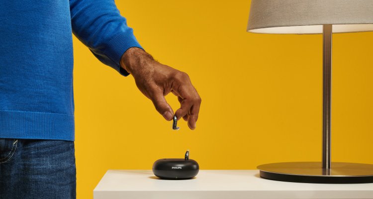 Philips HearLink şarj edilebilir işitme cihazlarını şarj cihazına yerleştiren adam. Tam gün işitme gücü için 3 saat şarj.