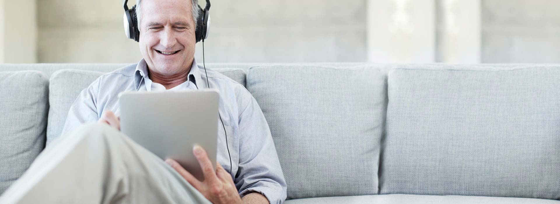 一位男士坐在沙發上，正在使用線上聽力測試檢查自己的聽力 